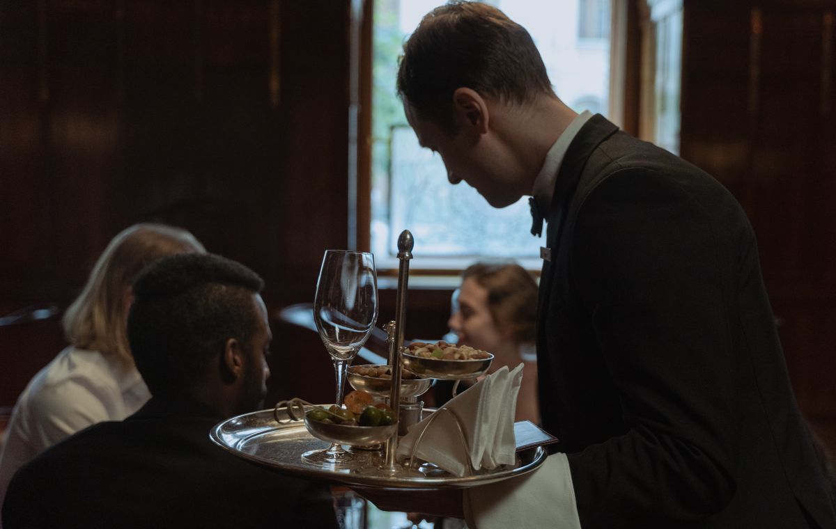 A server in a dark suit delivering plates in a fine-dining room.